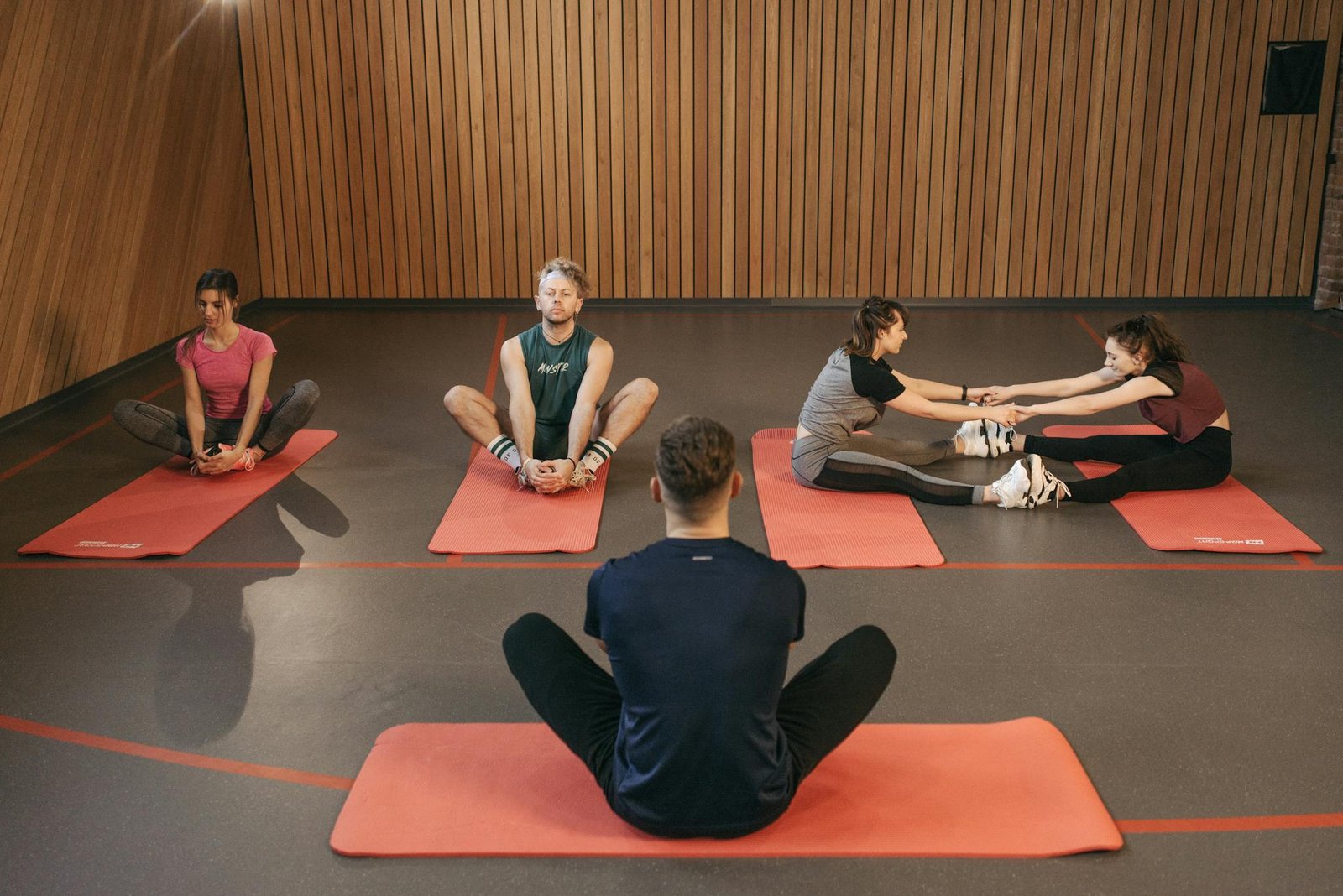 People engaging in a yoga class with red mats in an indoor wooden studio.